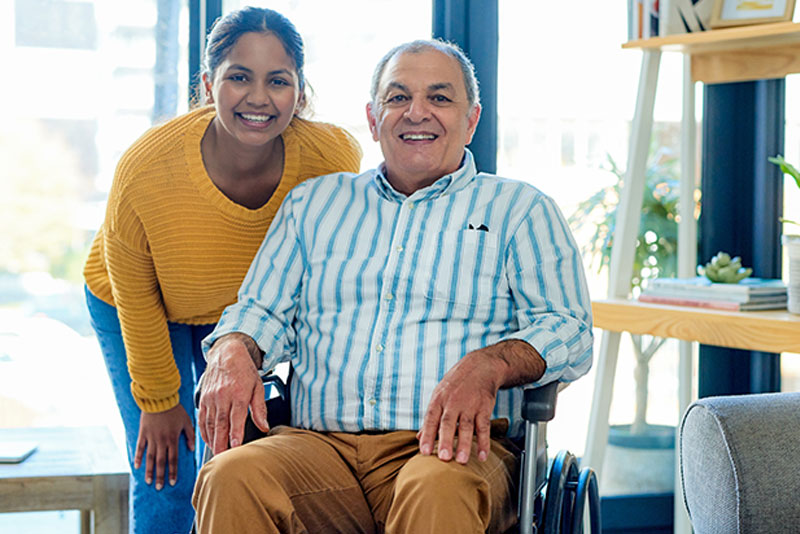 happy caregiver and senior disabled man smiling at camera