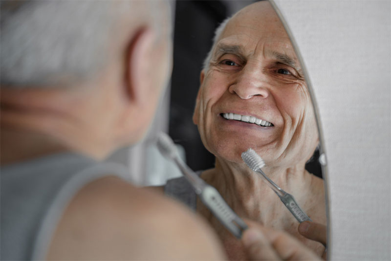 senior man looking in mirror brushing teeth