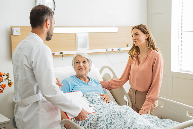 Woman serving as a senior advocate at the bedside of her elderly mother in the hospital, talking with the doctor