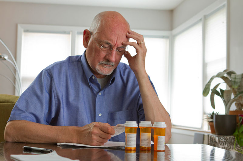 An older man reviews his medications to see if he takes any prescription drugs that raise the risk of falls.