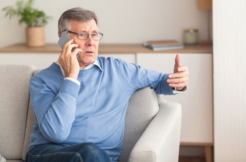 An older man knows about AI senior scams and is vigilant when speaking on the phone.